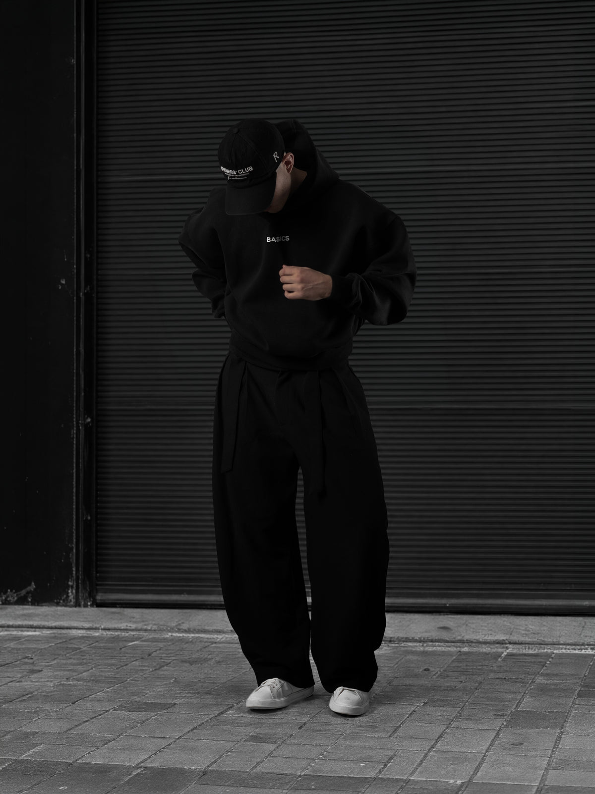 The Founders Hoodie negro en la calle, con la mano en el pecho